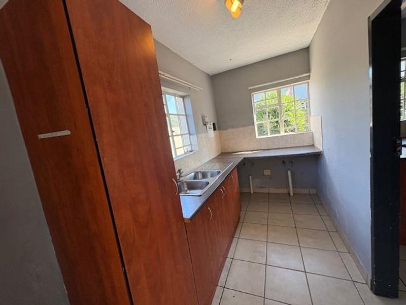 A functional kitchen space featuring built-in wooden cabinetry, a double basin sink, tiled splashbacks, and tiled flooring, offering a blank canvas for renovation.