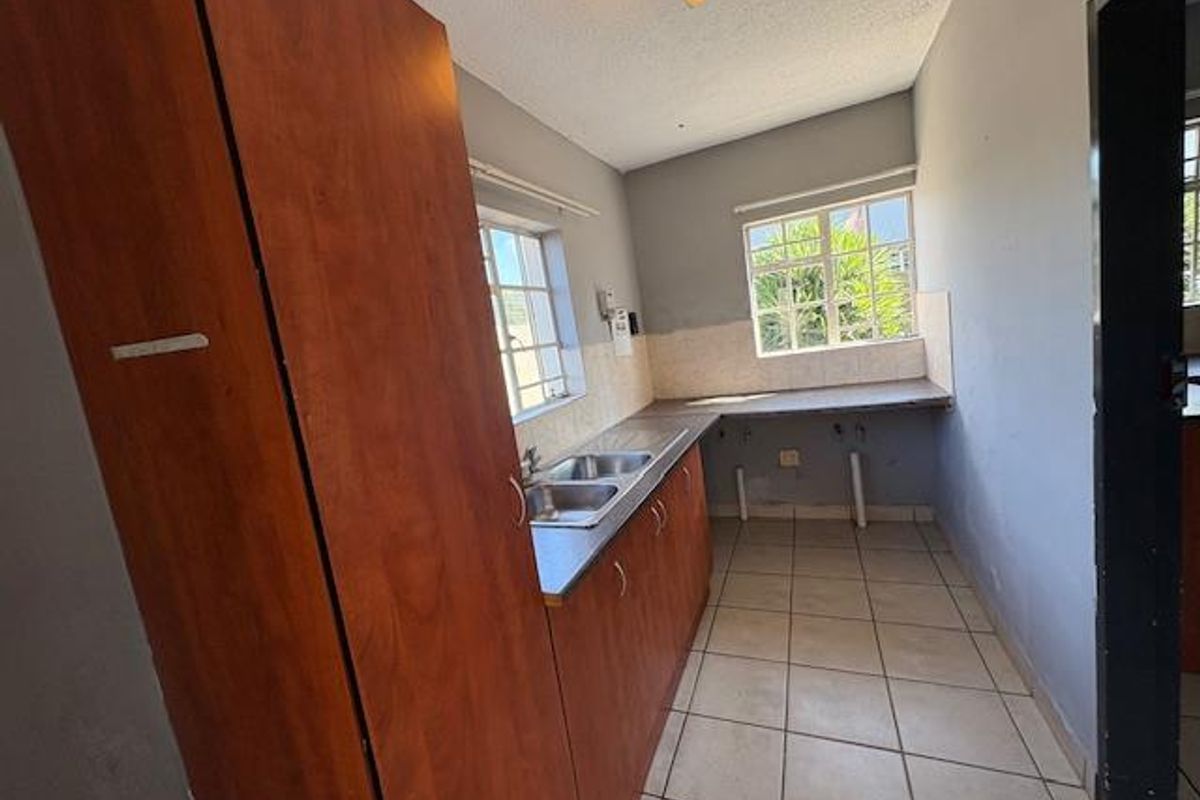 A functional kitchen space featuring built-in wooden cabinetry, a double basin sink, tiled splashbacks, and tiled flooring, offering a blank canvas for renovation.