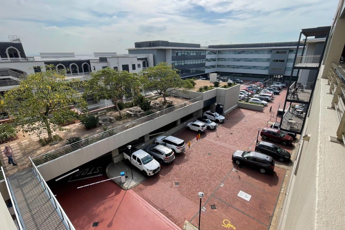 An elevated view of a commercial property featuring a multi-level parking area, paved driveway, and an integrated elevated garden terrace.