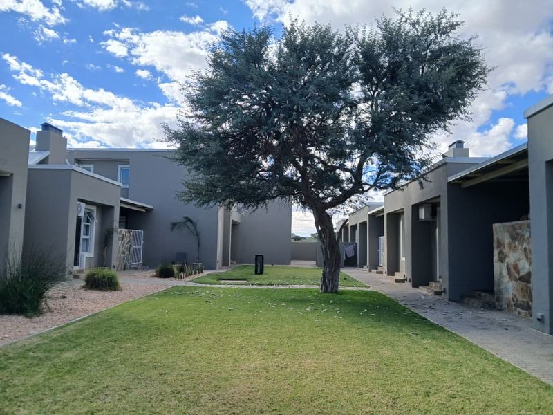 A well-maintained communal garden area between townhouse units, featuring a central mature tree, manicured lawn, and paved pathways.