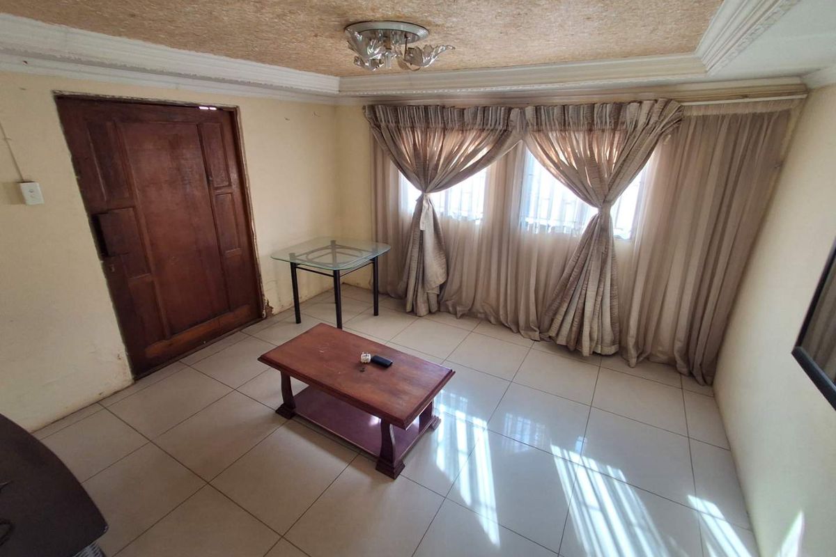 A living room featuring tiled flooring, textured ceiling with crown molding, and window security bars. The space requires cosmetic updates to improve its overall condition.