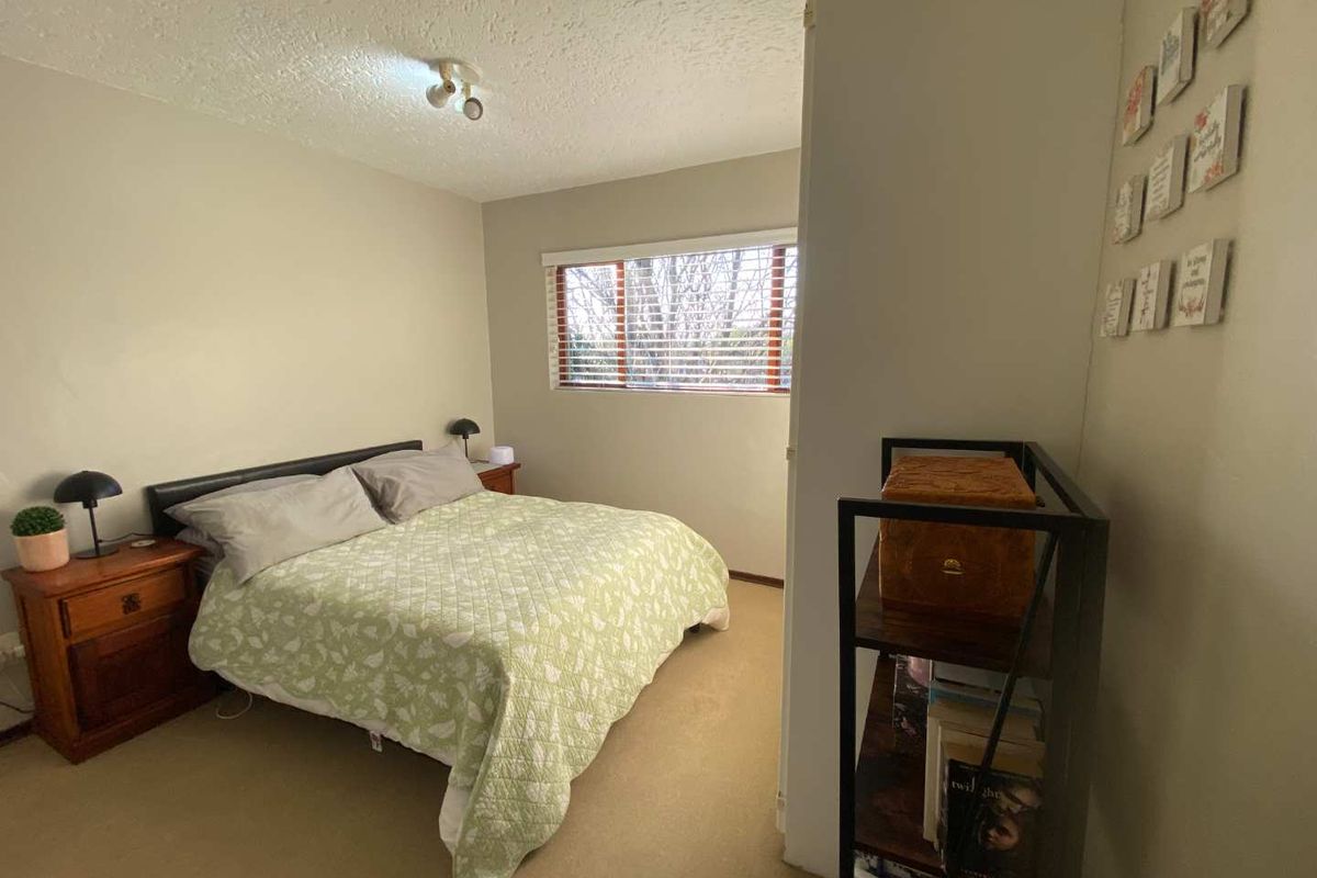 A standard bedroom featuring carpet flooring, a textured ceiling, and a window with fitted blinds.