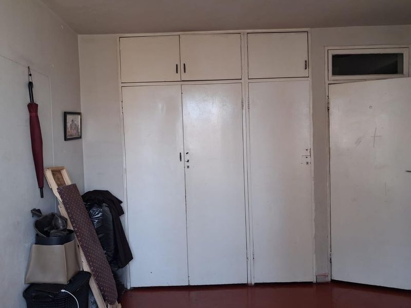A bedroom featuring built-in floor-to-ceiling cupboards with overhead storage and a standard internal door, requiring cosmetic updates to the paint and finishes.