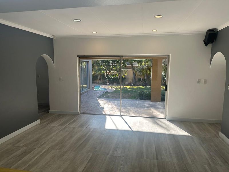 Spacious living area featuring modern laminate flooring, recessed lighting, and large sliding glass doors providing direct access to the rear patio and pool area.