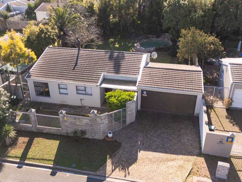 Aerial view of a residential property featuring a tiled roof house, paved driveway, attached garage, perimeter walling, and a rear swimming pool.