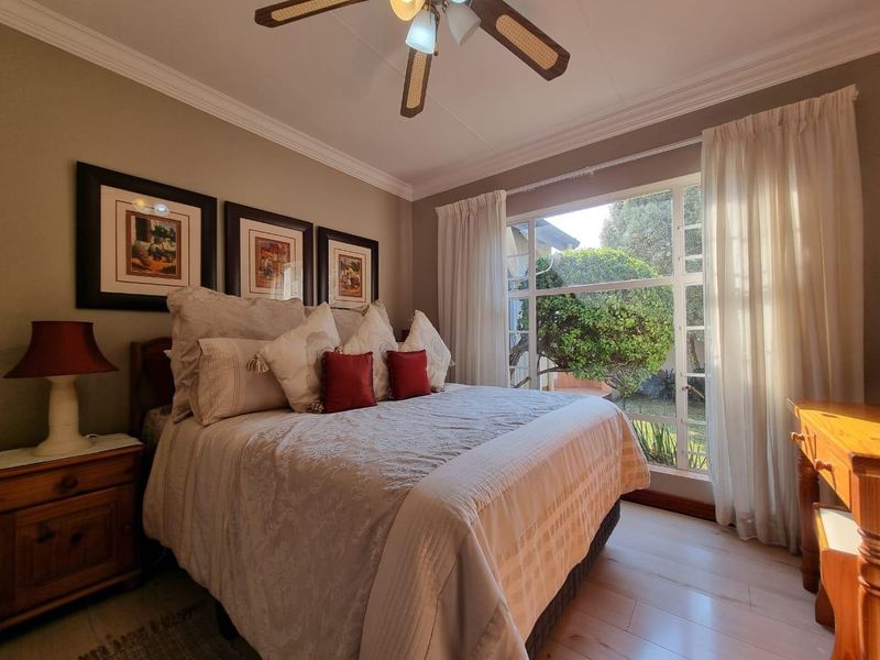 A well-maintained bedroom featuring laminate flooring, crown molding, a ceiling fan, and a large window providing natural light and garden views.