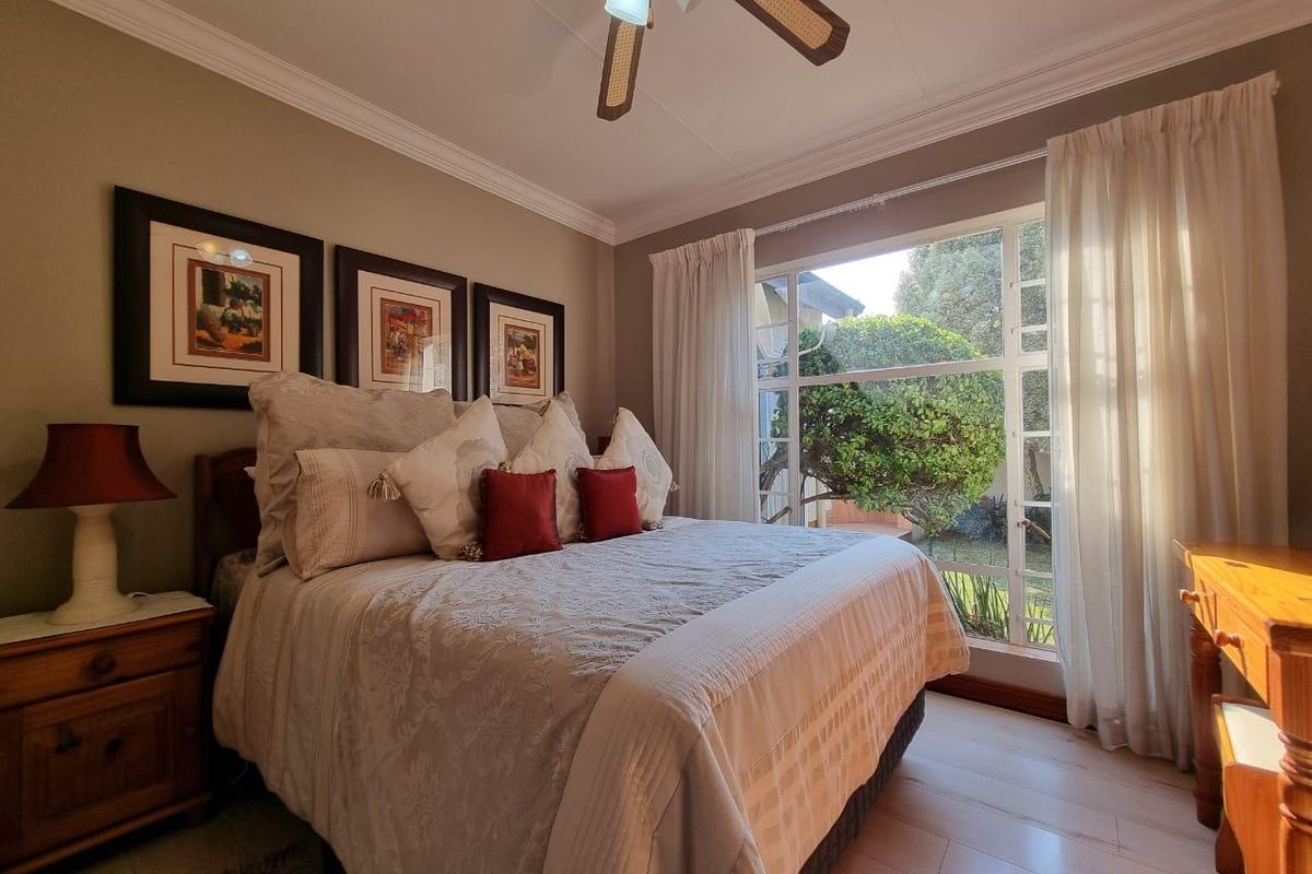 A well-maintained bedroom featuring laminate flooring, crown molding, a ceiling fan, and a large window providing natural light and garden views.
