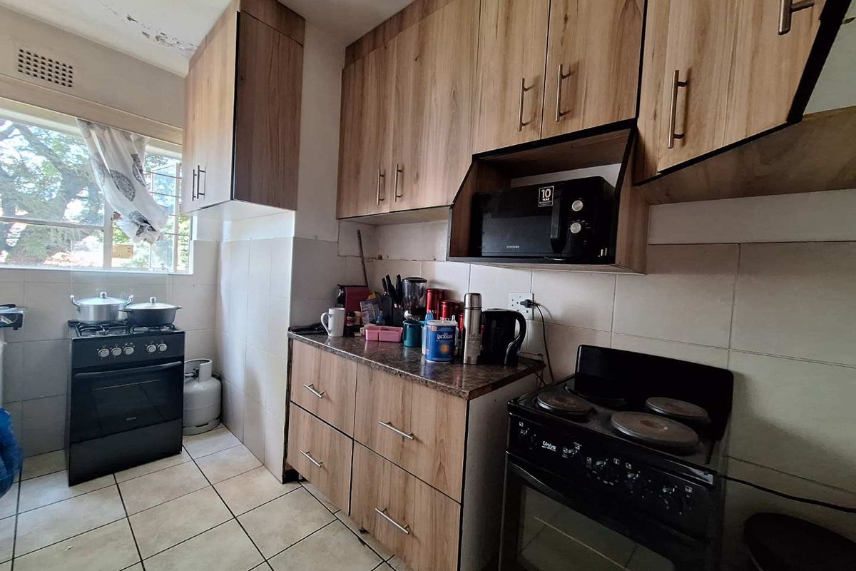 A functional kitchen featuring wood-look cabinetry, tiled splashbacks, tiled flooring, and two freestanding stoves.