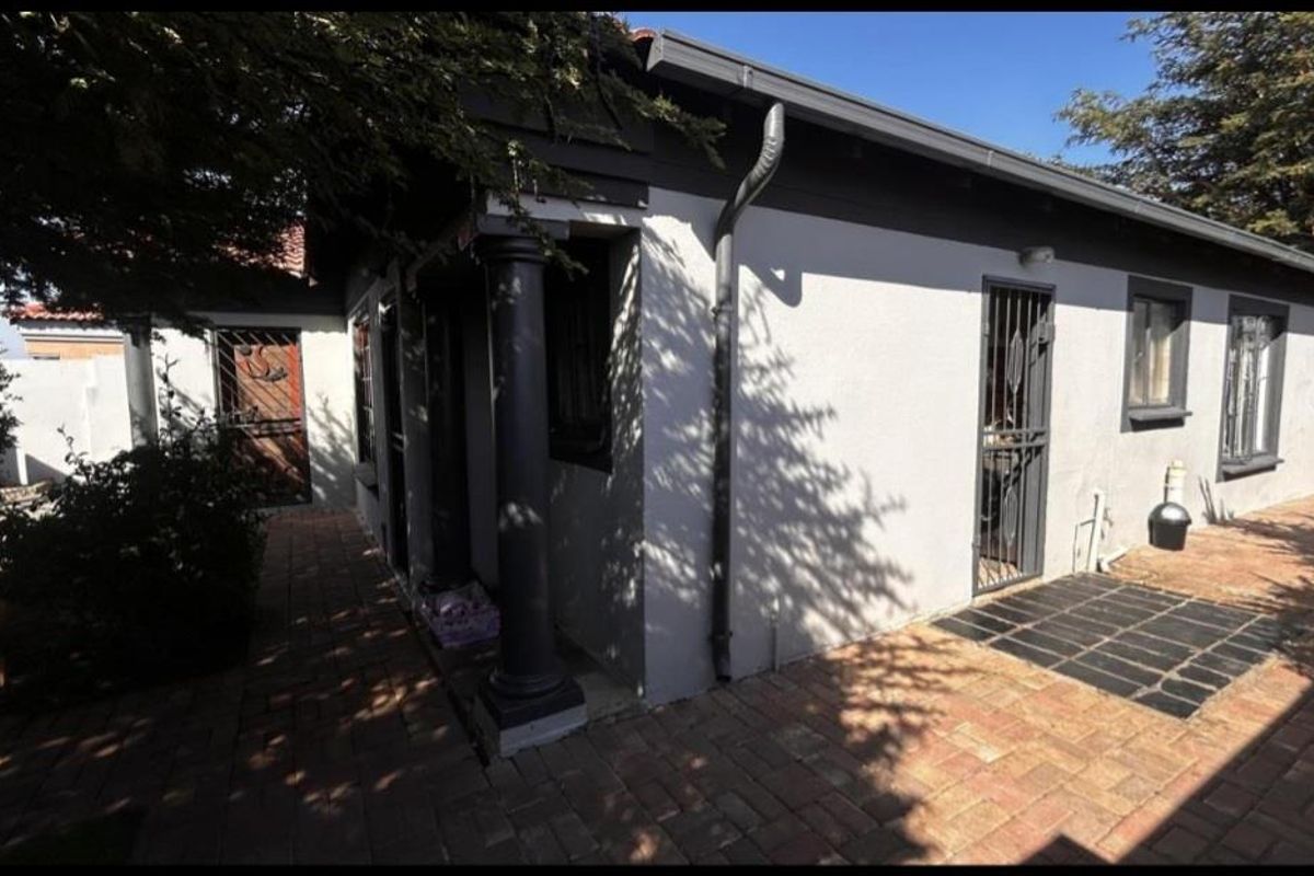 Exterior view of the property featuring a paved walkway, covered entrance with decorative columns, and security gates on doors and windows.