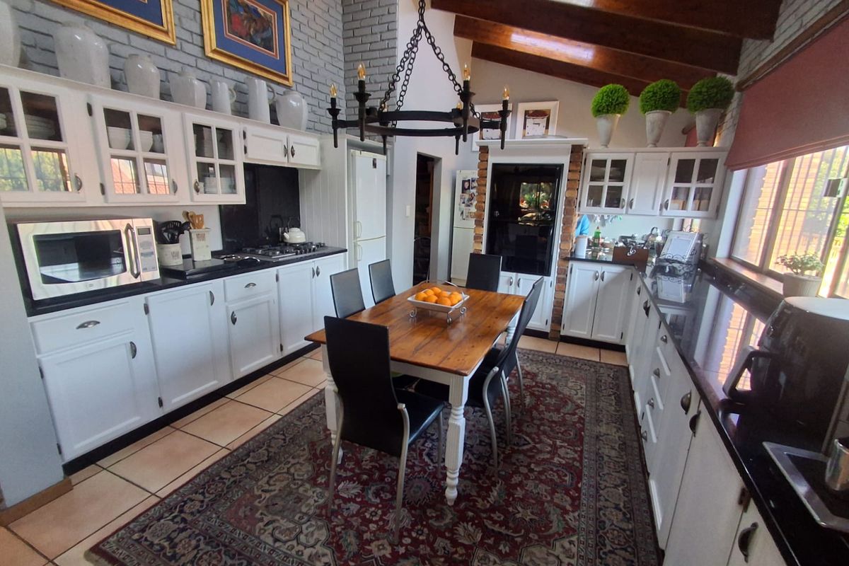 Spacious kitchen featuring white cabinetry, granite countertops, exposed timber ceiling beams, and a brick feature wall, creating a warm and functional cooking space.