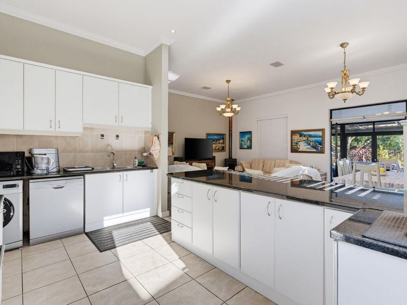 Open-plan kitchen and living area featuring white cabinetry, granite countertops, tiled flooring, and direct access to an outdoor patio space.