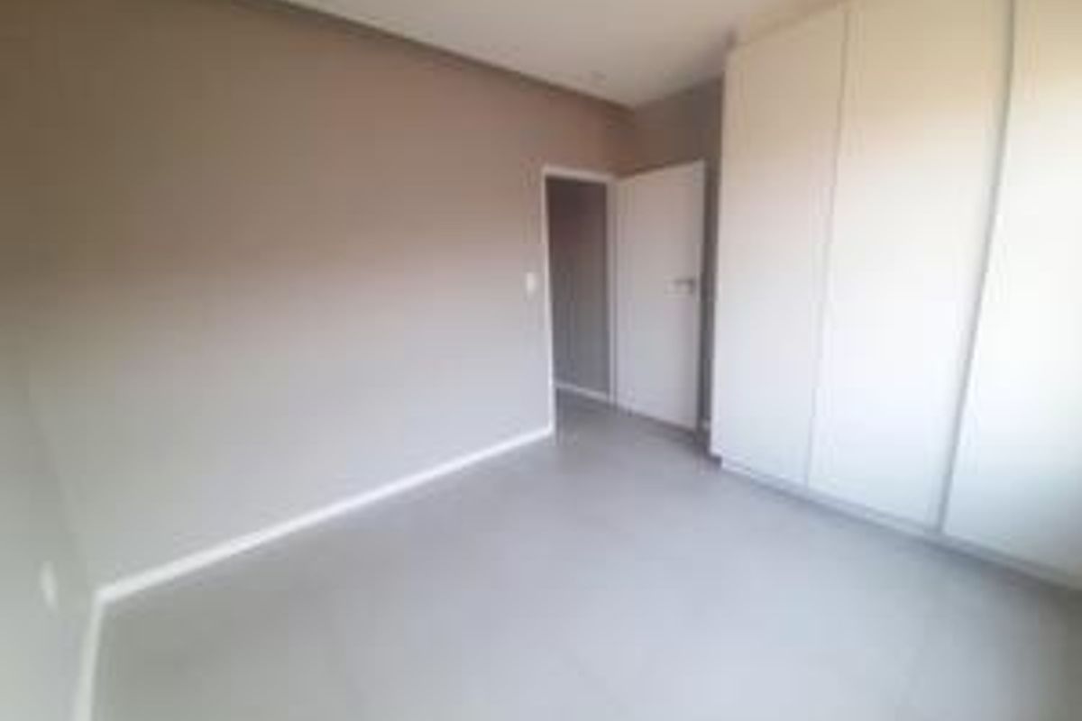 A clean, empty bedroom featuring neutral wall tones, tiled flooring, and built-in cupboards, offering a versatile space ready for personalization.