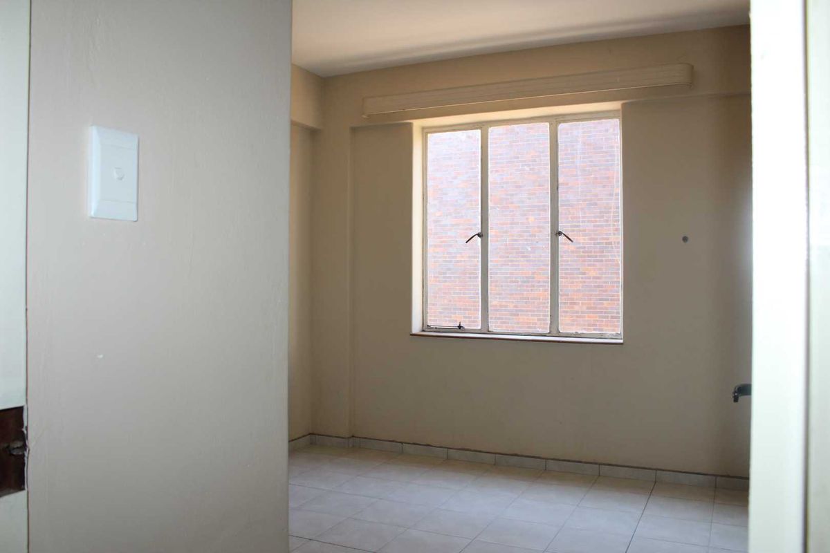 An empty bedroom featuring tiled flooring and a large metal-framed window, offering a blank canvas for potential interior design updates.