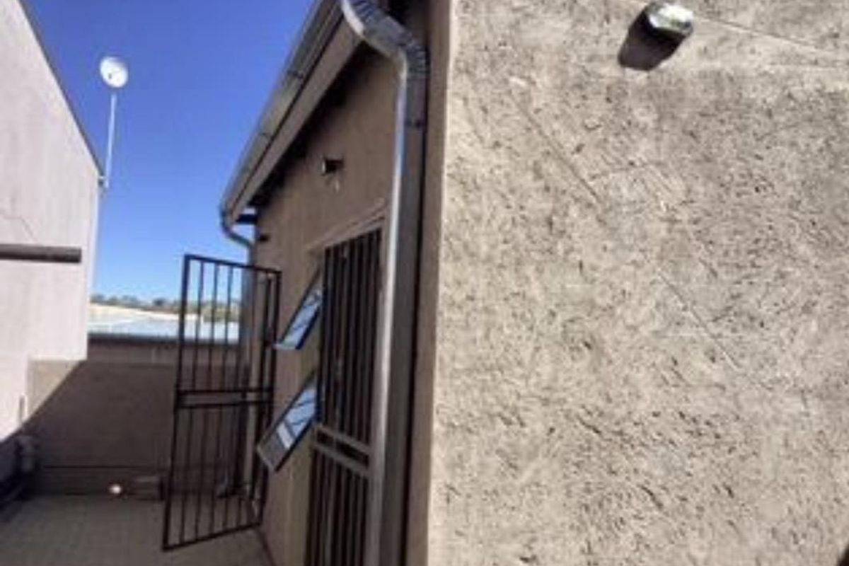A view of the rear exterior area featuring a textured wall, security gates, and functional downpipe drainage system.