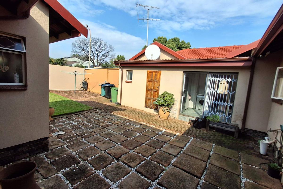 A paved rear courtyard area featuring a brick-paved section, lawn, and access to the main dwelling via sliding doors with security gates.