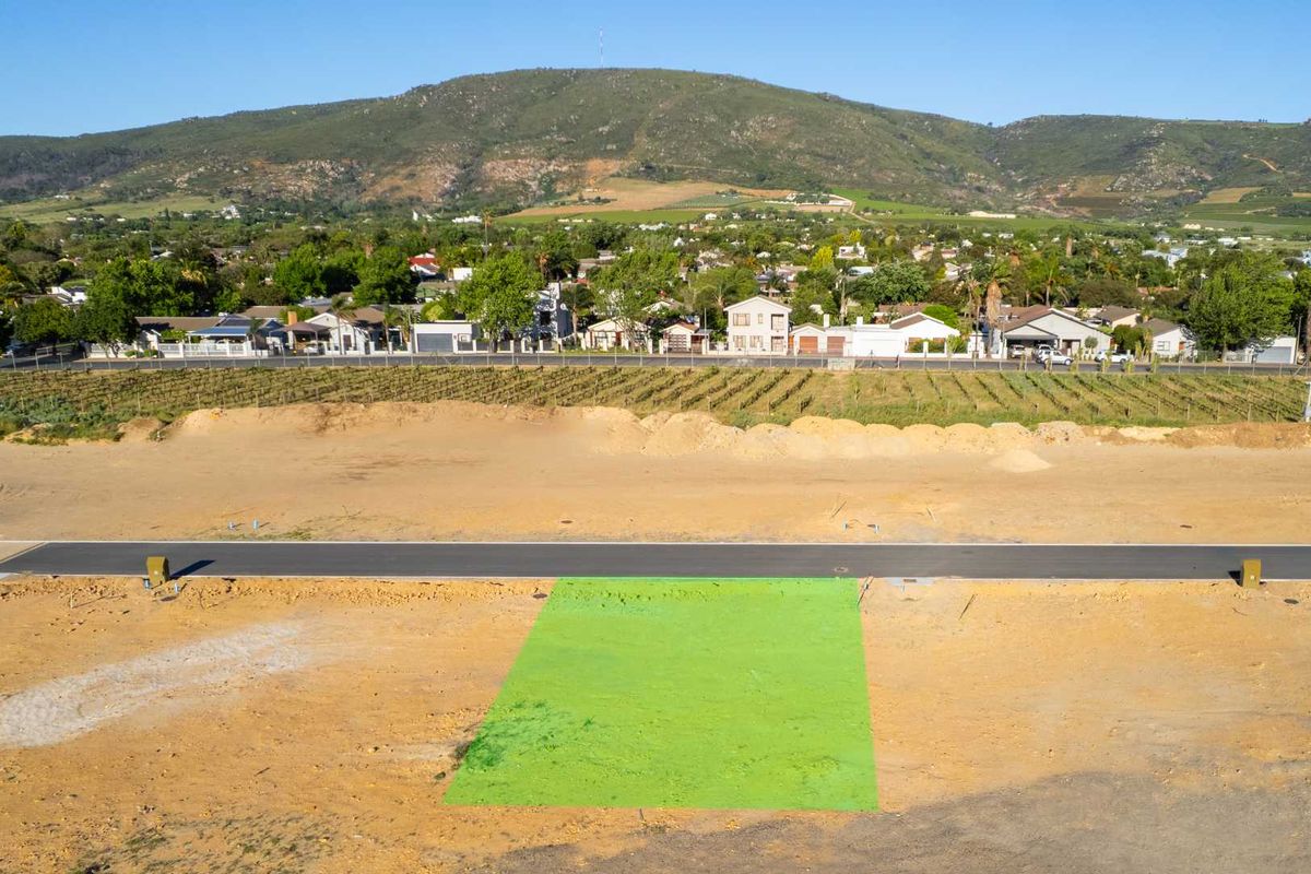An aerial view of a vacant residential plot featuring a highlighted area, paved road access, and scenic mountain views in the background.