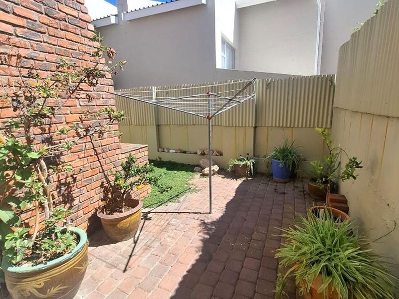 A private rear courtyard featuring brick paving, a brick feature wall, and a functional rotary clothesline enclosed by corrugated metal fencing.