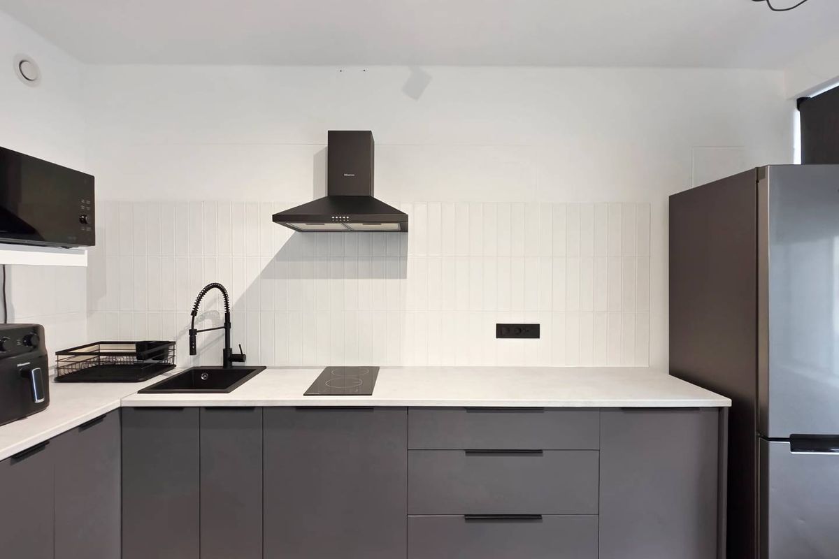 Modern kitchen featuring sleek grey cabinetry, white stone countertops, a black sink with matching tapware, induction hob, and integrated extractor fan.
