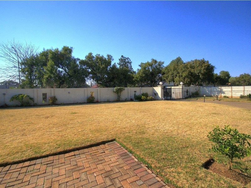 A spacious, level garden area featuring a perimeter wall with electric fencing, a metal gate, and a brick-paved patio section.