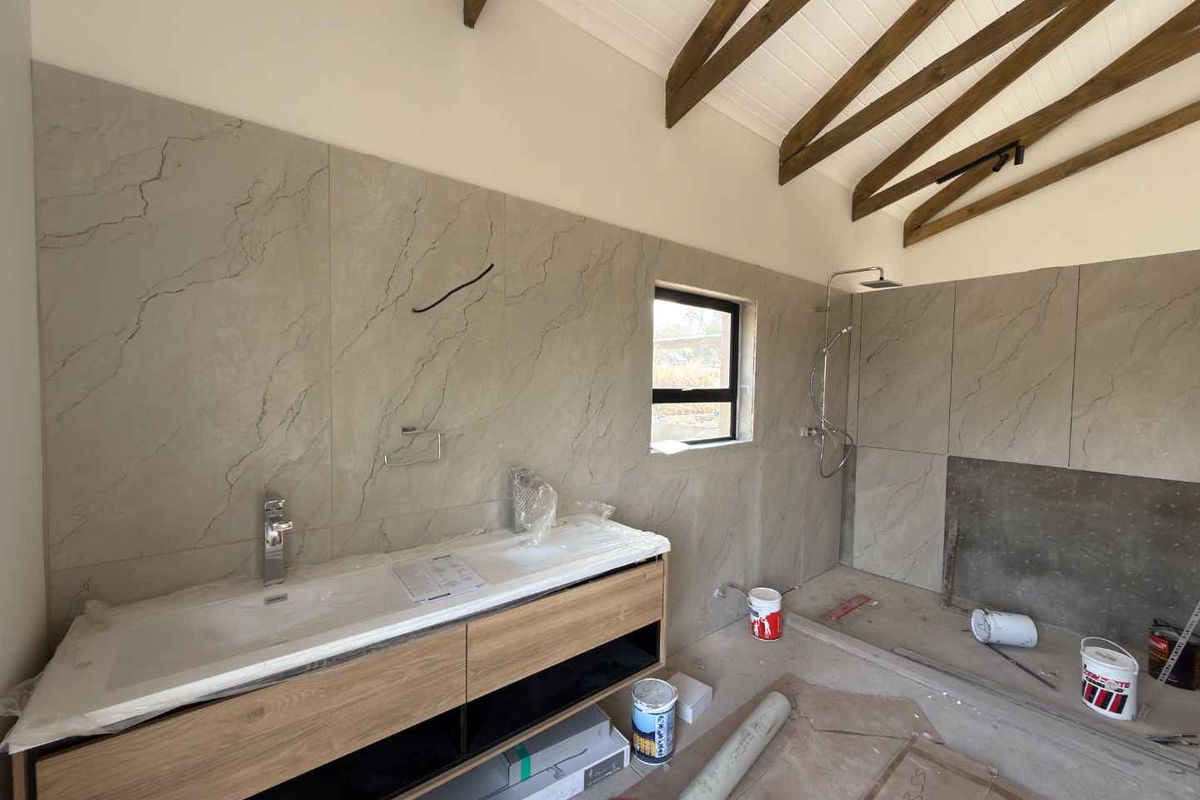 A modern bathroom under construction featuring a floating vanity, walk-in shower, and vaulted ceiling with exposed timber beams, currently awaiting final finishes.