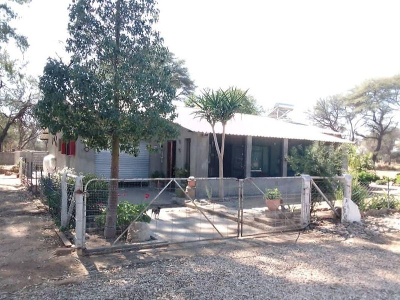 Front view of a small holding property featuring a metal roof, solar geyser, and a fenced yard with a concrete patio area.