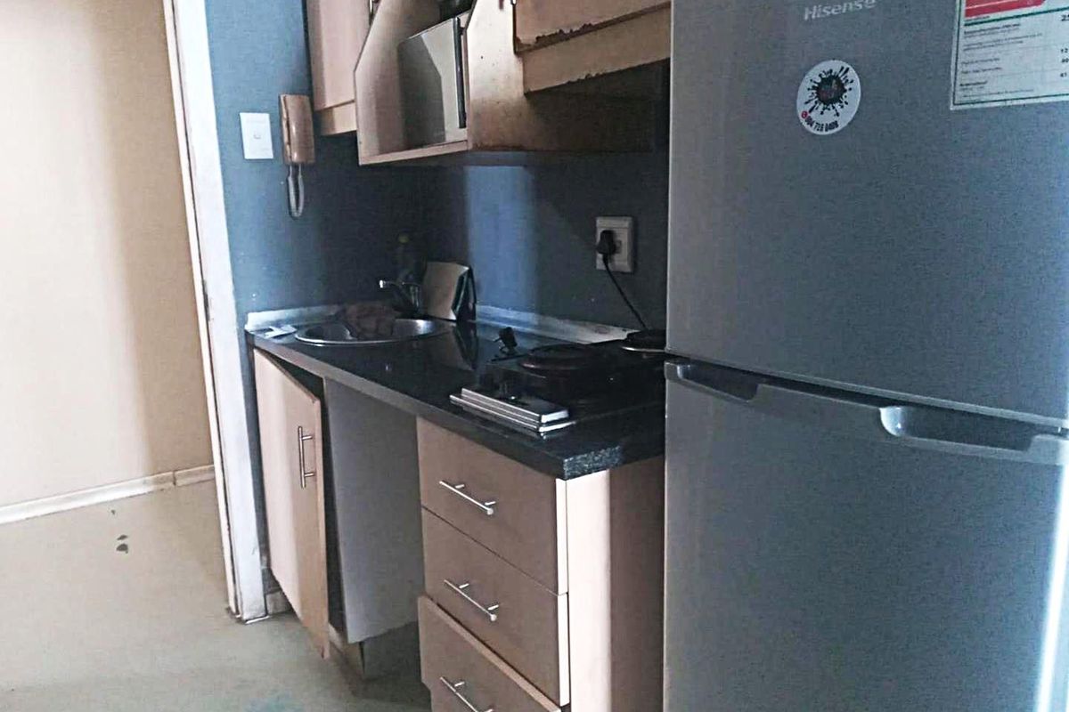 Compact kitchen area featuring built-in cabinetry, a laminate countertop, and a stainless steel sink, showing signs of wear and requiring maintenance.