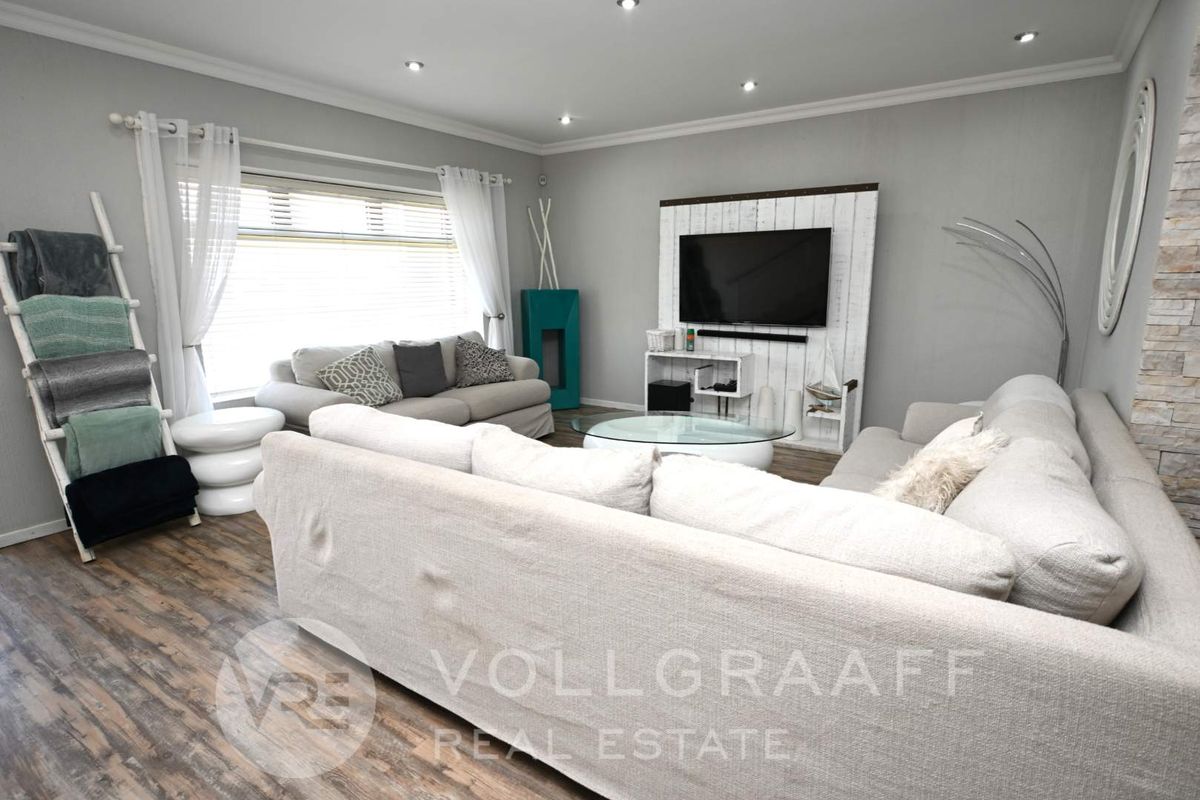 A well-maintained living room featuring recessed ceiling lighting, wood-look flooring, and a feature wall with stone cladding accents.
