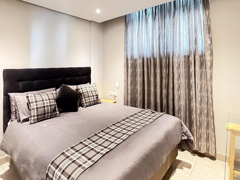 A well-maintained bedroom featuring neutral wall finishes, tiled flooring, and floor-to-ceiling window treatments.