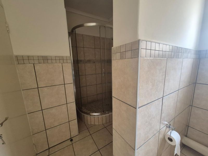 A functional bathroom featuring a corner shower enclosure with tiled walls and flooring throughout.