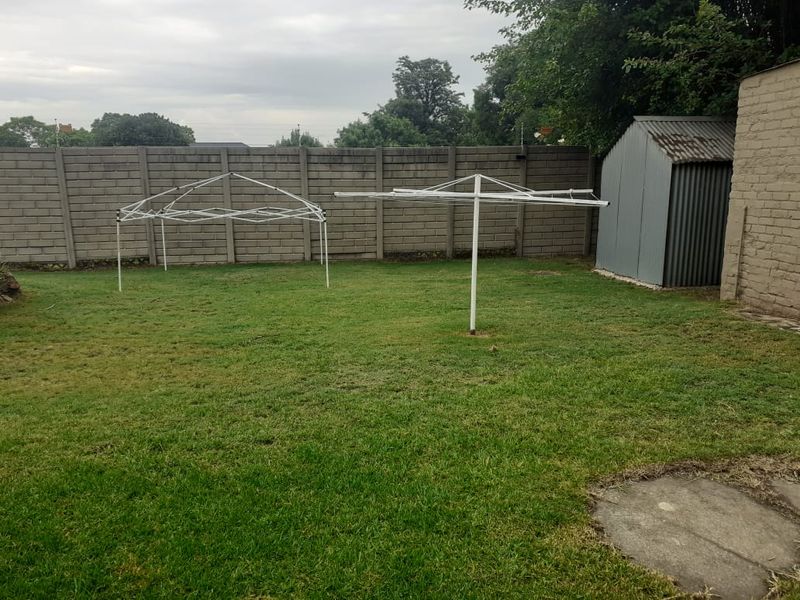 A spacious rear garden featuring a lawn, a precast concrete boundary wall, a metal storage shed, and a rotary clothesline.