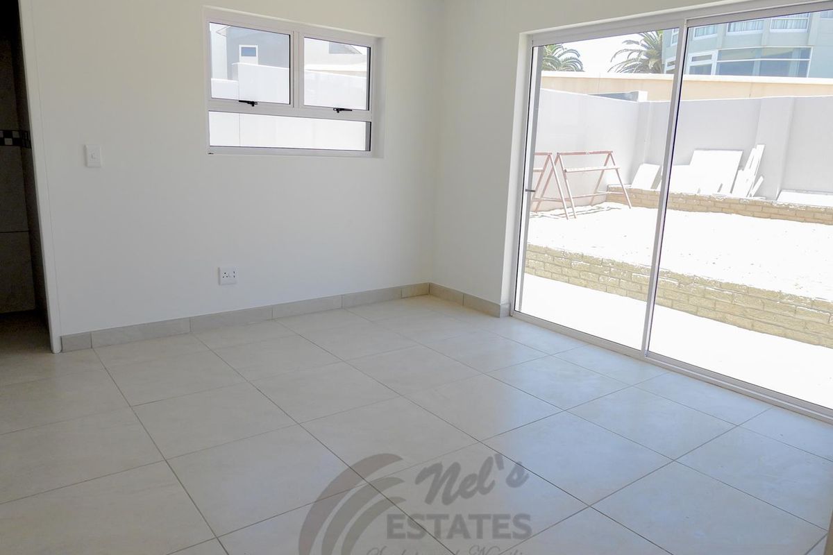 A bright, empty living room featuring large sliding glass doors that open to a private rear courtyard area.