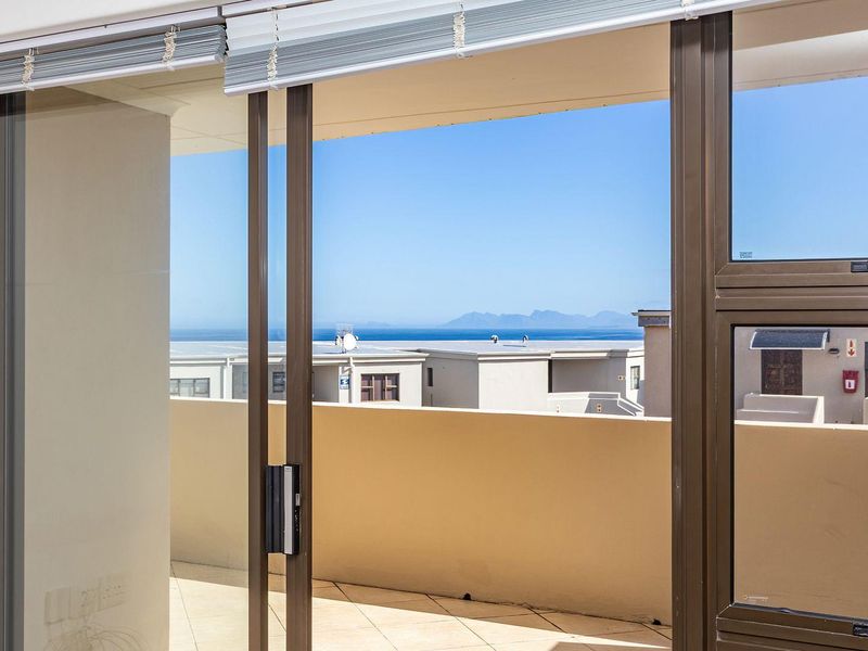 A spacious balcony featuring tiled flooring and sliding glass doors, offering clear views of the surrounding neighborhood and distant ocean.