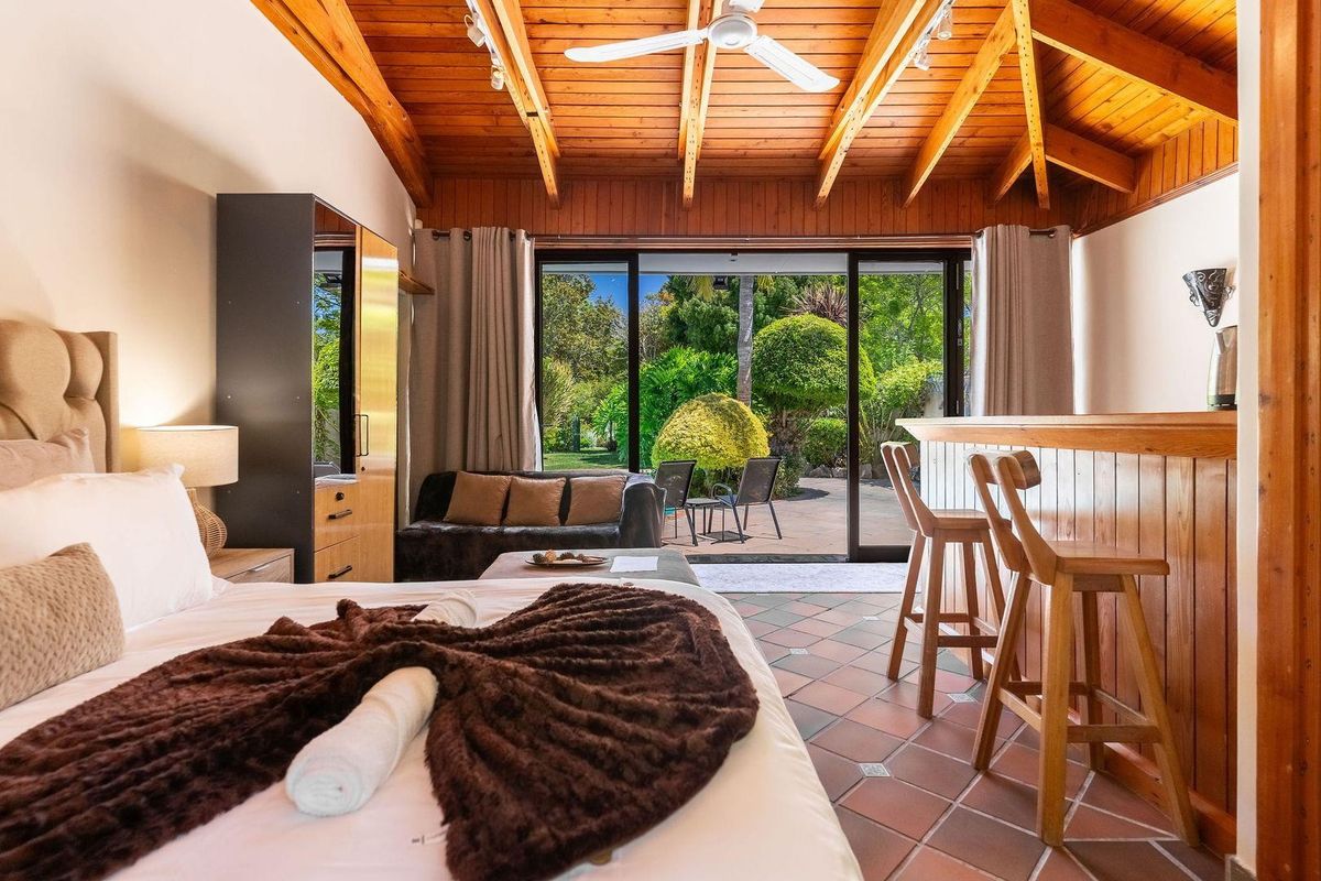 Spacious bedroom featuring a vaulted timber ceiling, tiled flooring, and large sliding glass doors opening onto a private garden patio.