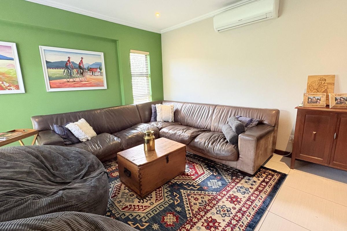 A comfortable living room featuring tiled flooring, a wall-mounted air conditioning unit, and a vibrant green accent wall.