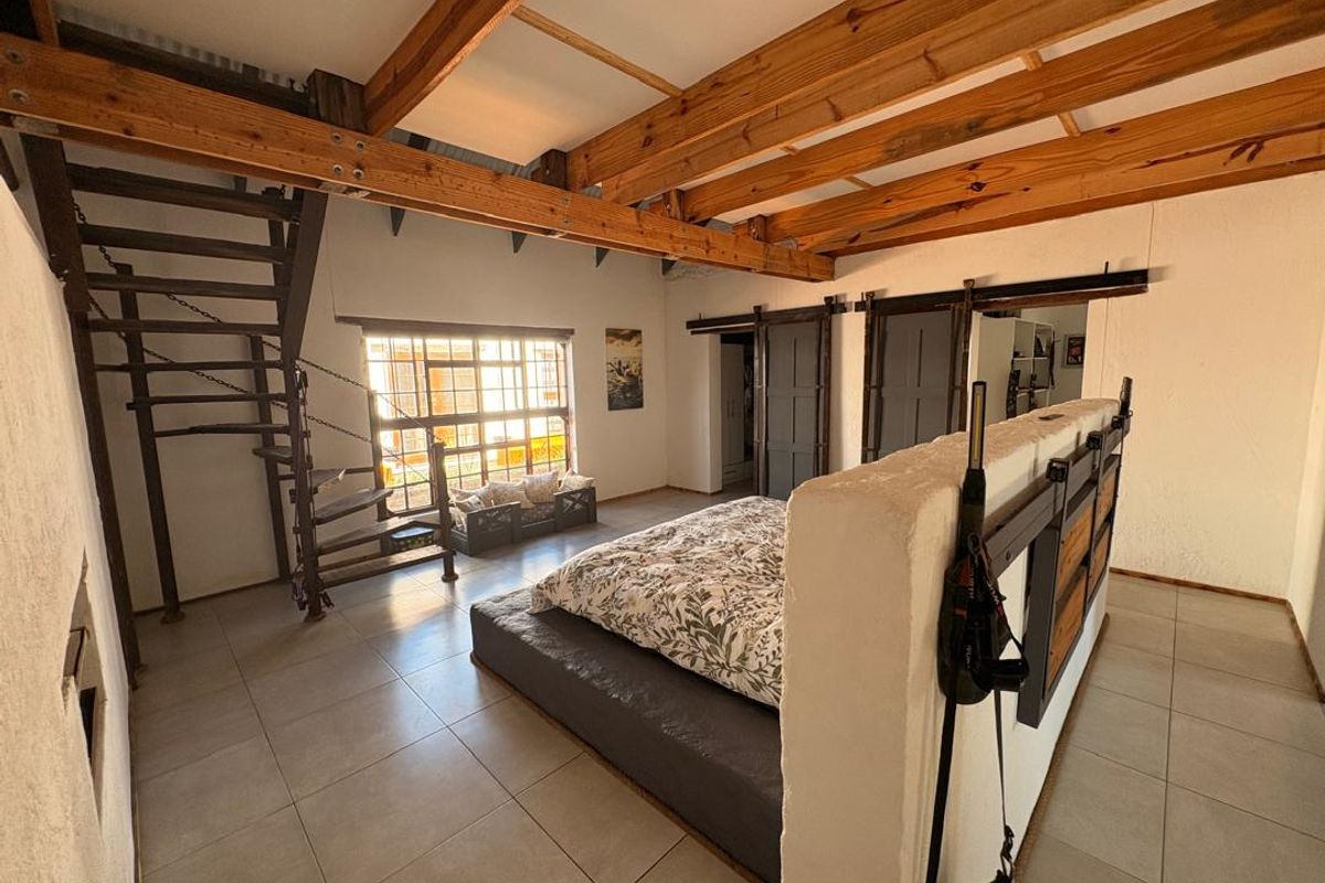 Spacious bedroom featuring exposed timber ceiling beams, a unique metal spiral staircase, tiled flooring, and sliding barn-style doors with a central partition wall.