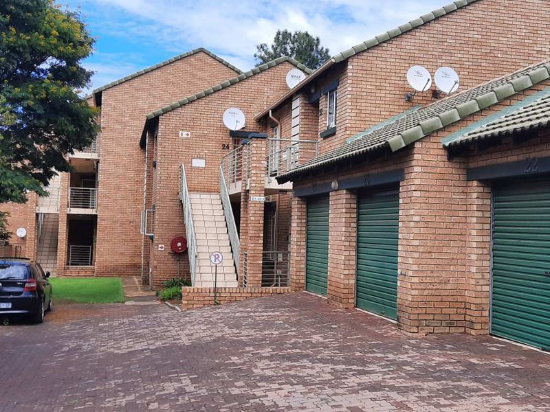 Front view of a face brick townhouse complex featuring multiple roller shutter garages, paved driveway, and external staircase access to upper levels.
