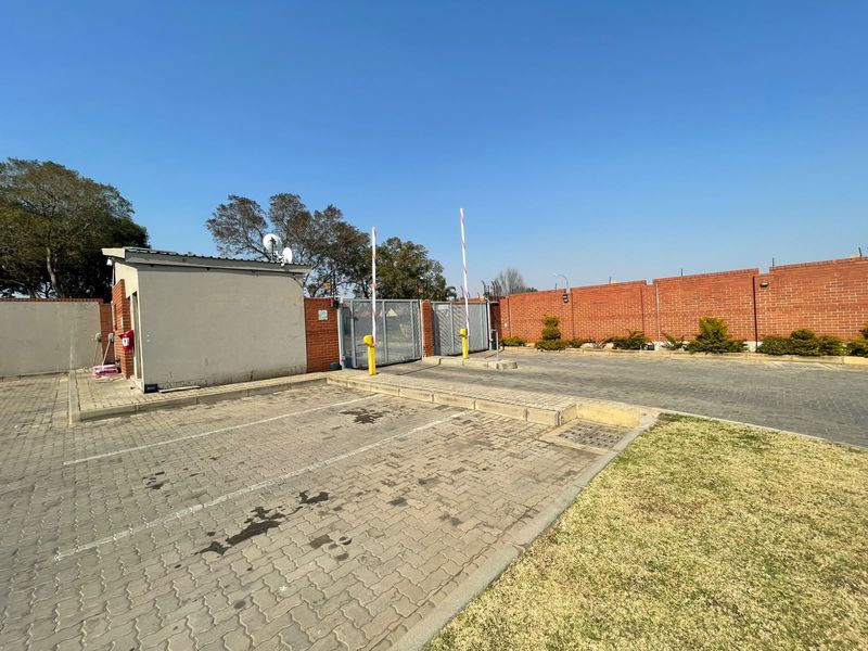 A secure apartment complex entrance featuring a paved driveway, guard house, and automated boom gate access control.