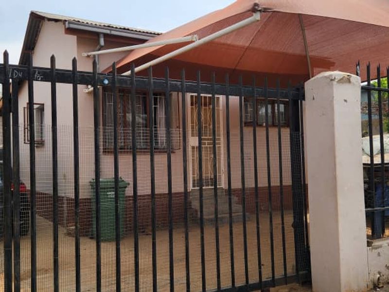 Front exterior view of a residential property featuring a metal security fence, shade sail, and concrete driveway area.