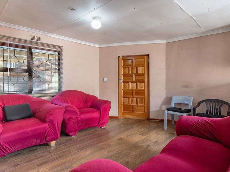 A living room featuring laminate flooring, a timber door, and security window blinds, requiring cosmetic updates to the ceiling and wall finishes.