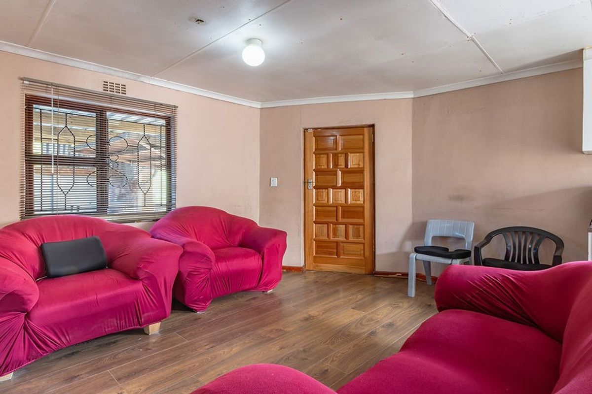 A living room featuring laminate flooring, a timber door, and security window blinds, requiring cosmetic updates to the ceiling and wall finishes.