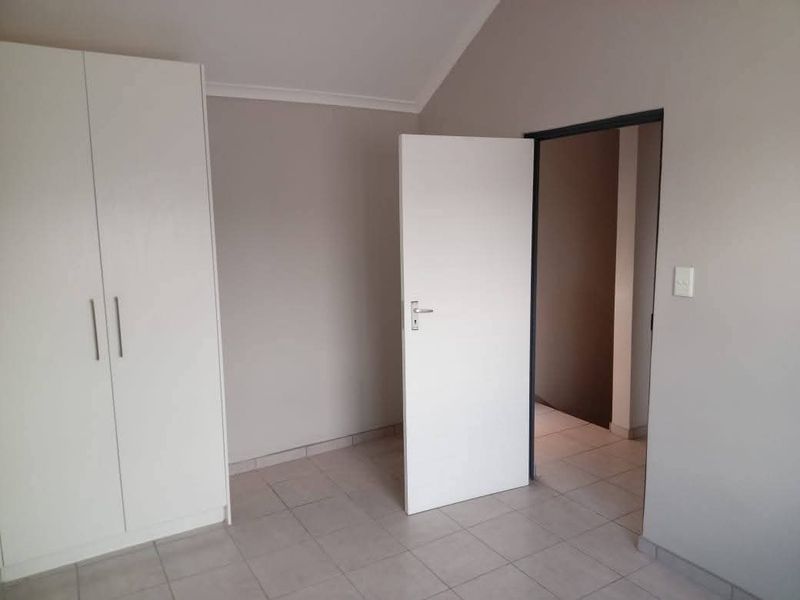 A clean, empty bedroom featuring neutral wall tones, tiled flooring, and a built-in wardrobe, offering a versatile space ready for personalization.