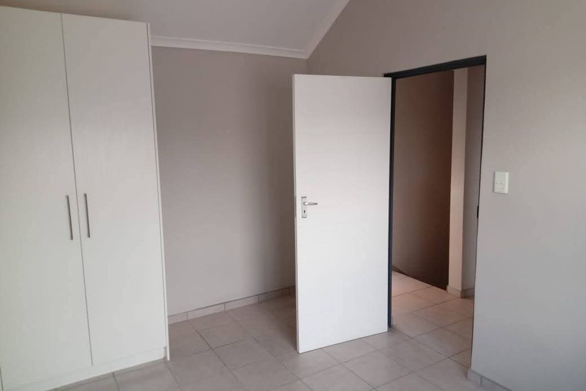 A clean, empty bedroom featuring neutral wall tones, tiled flooring, and a built-in wardrobe, offering a versatile space ready for personalization.