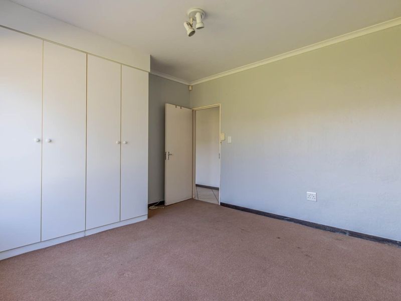 A spacious, empty bedroom featuring built-in cupboards, neutral wall finishes, and carpeted flooring, offering a blank canvas for personalization.