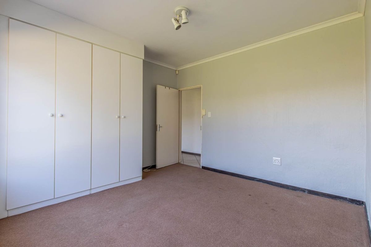 A spacious, empty bedroom featuring built-in cupboards, neutral wall finishes, and carpeted flooring, offering a blank canvas for personalization.
