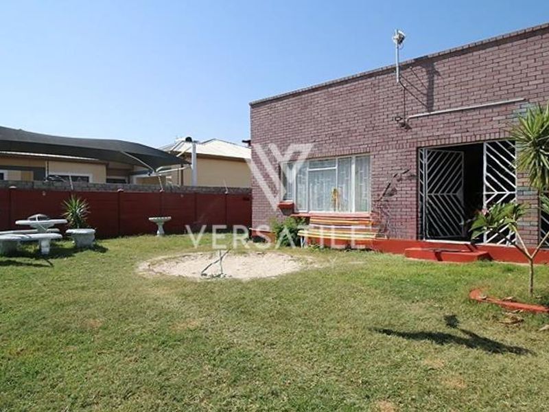 Rear view of the property featuring a brick facade, security gates, and a private garden area with a lawn.