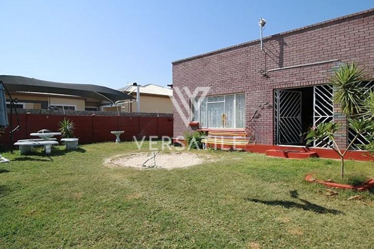 Rear view of the property featuring a brick facade, security gates, and a private garden area with a lawn.
