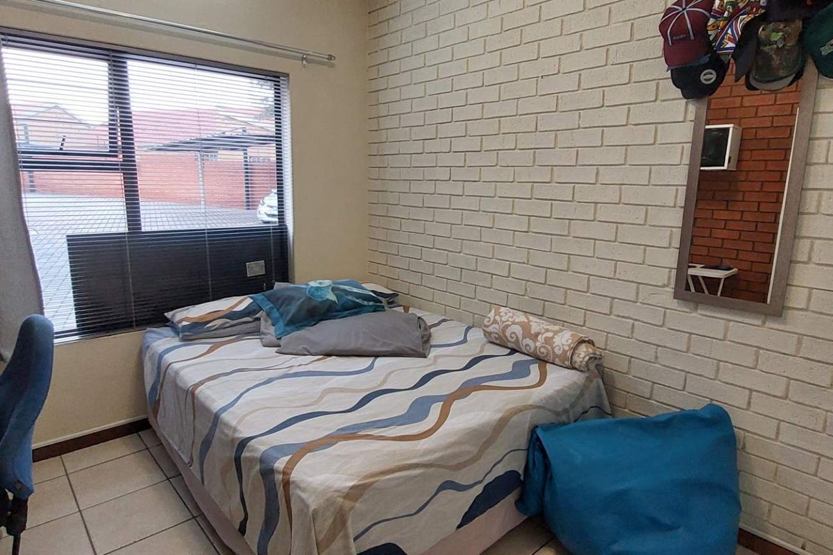 A bedroom featuring a painted brick feature wall, tiled flooring, and a large window with horizontal blinds.