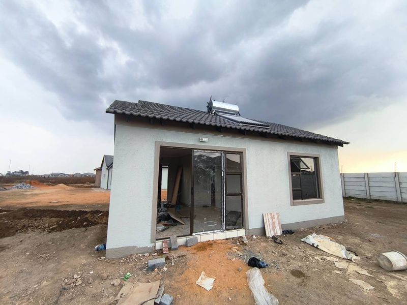 Rear view of a newly constructed house featuring a tiled roof, solar water heater, and aluminium sliding doors, set on an undeveloped plot.