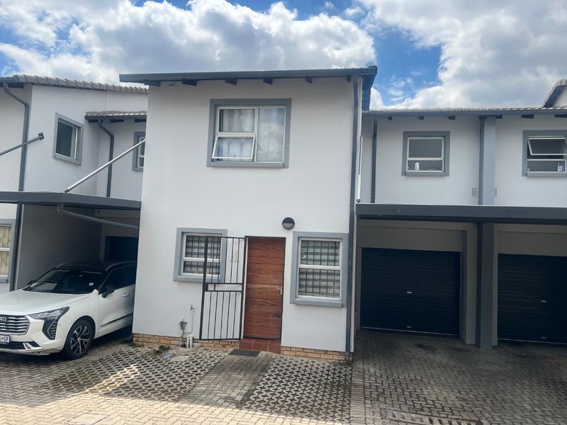 Front elevation of a two-story apartment unit featuring a paved driveway, integrated garage, and secure entrance with a wooden door.