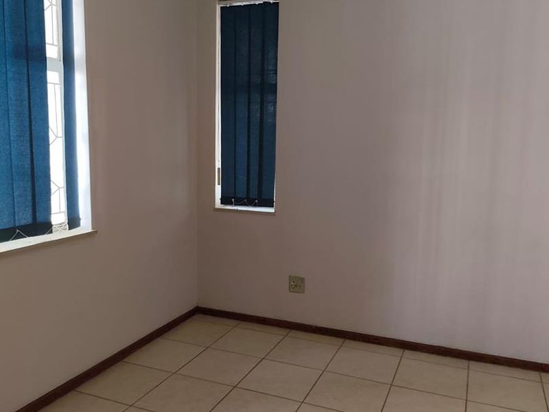 A clean, empty bedroom featuring neutral wall paint, tiled flooring, and vertical window blinds, offering a versatile space ready for personalization.